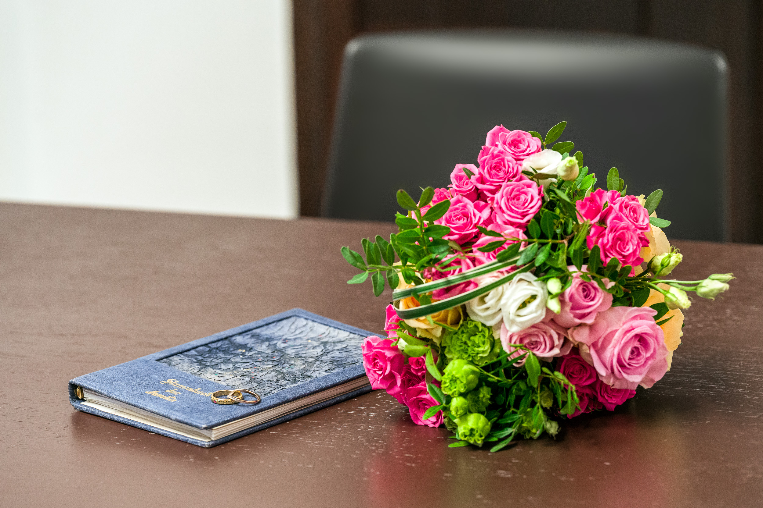 Blumenstrauß mit rosanen Rosen liegt neben einem Familienstammbuch auf einem dunklen Holztisch